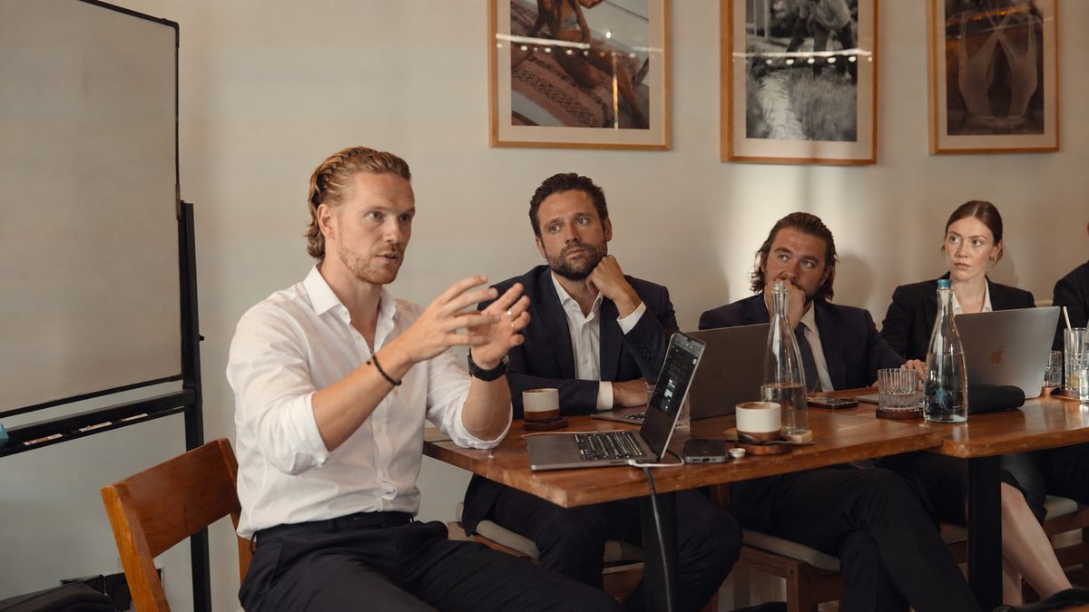 A training session at Mastermind #2: the host explains while three participants with laptops listen at a long table.